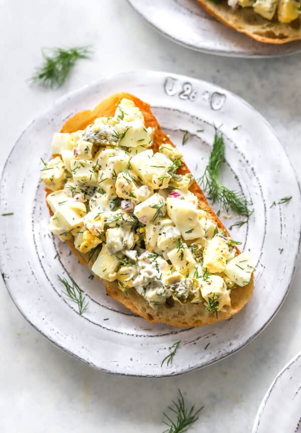 Egg salad with fresh herbs on toasted bread on a round plate.