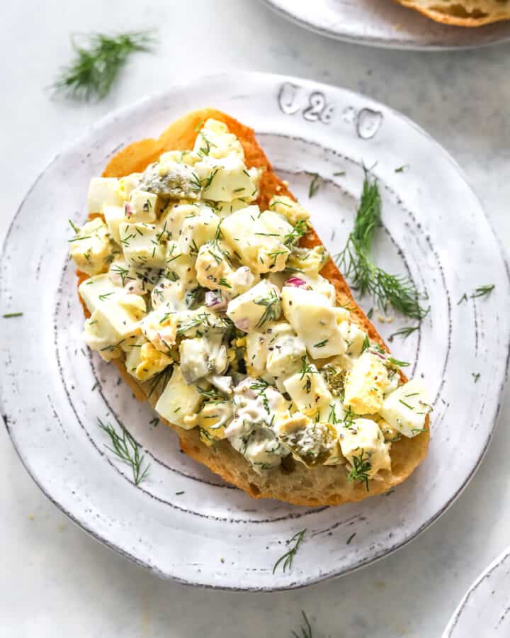 Egg salad with fresh herbs on toasted bread on a round plate.