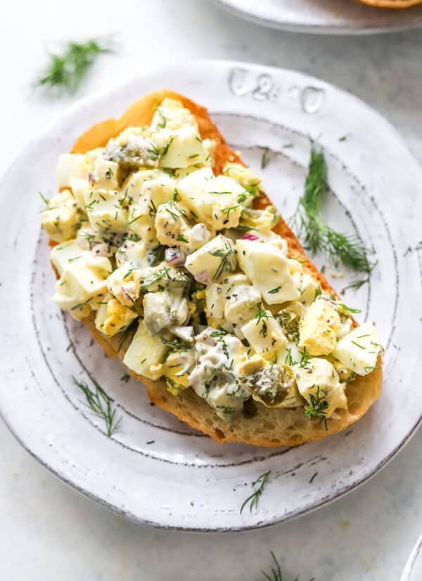 Creamy, herby egg salad on toast on a round plate sprinkled with dill.