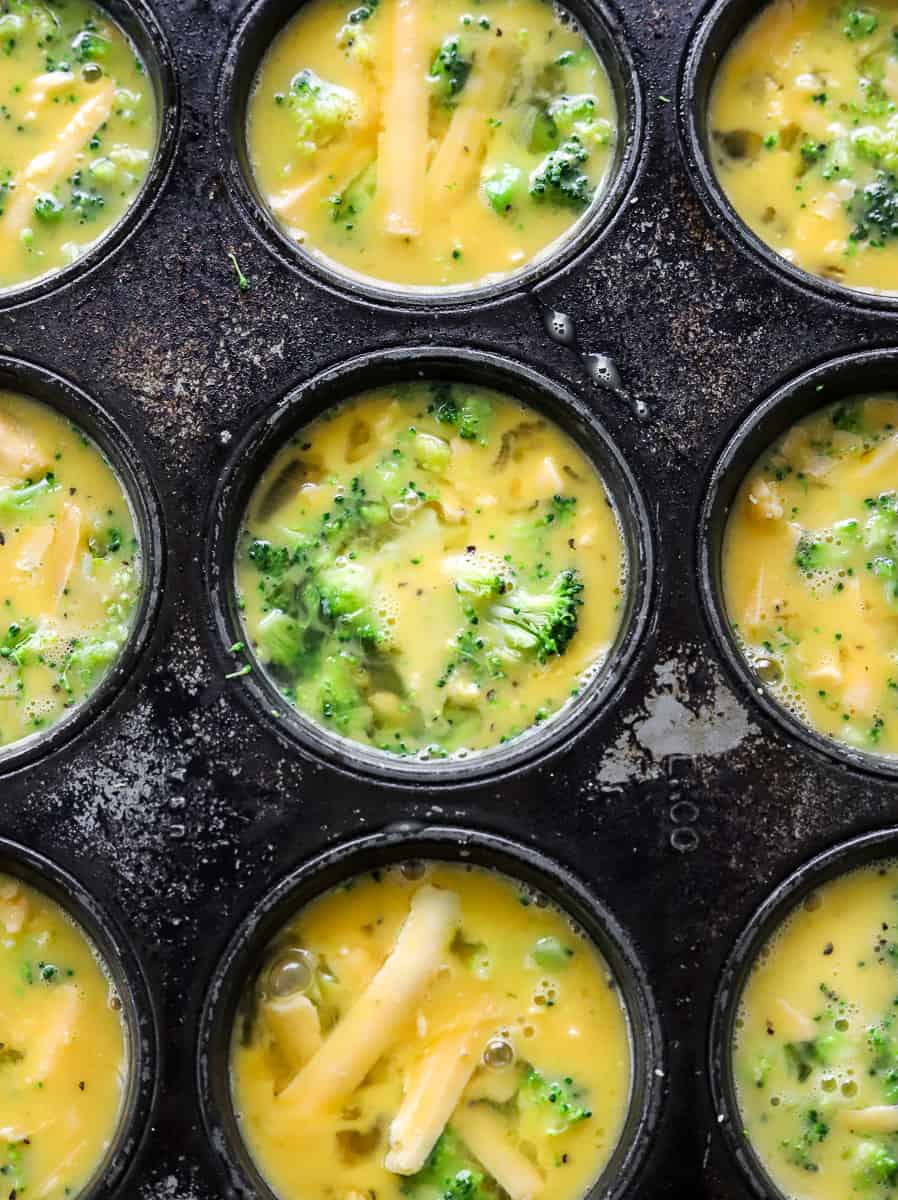 Uncooked egg filled broccoli and cheddar quiche in a muffin pan.