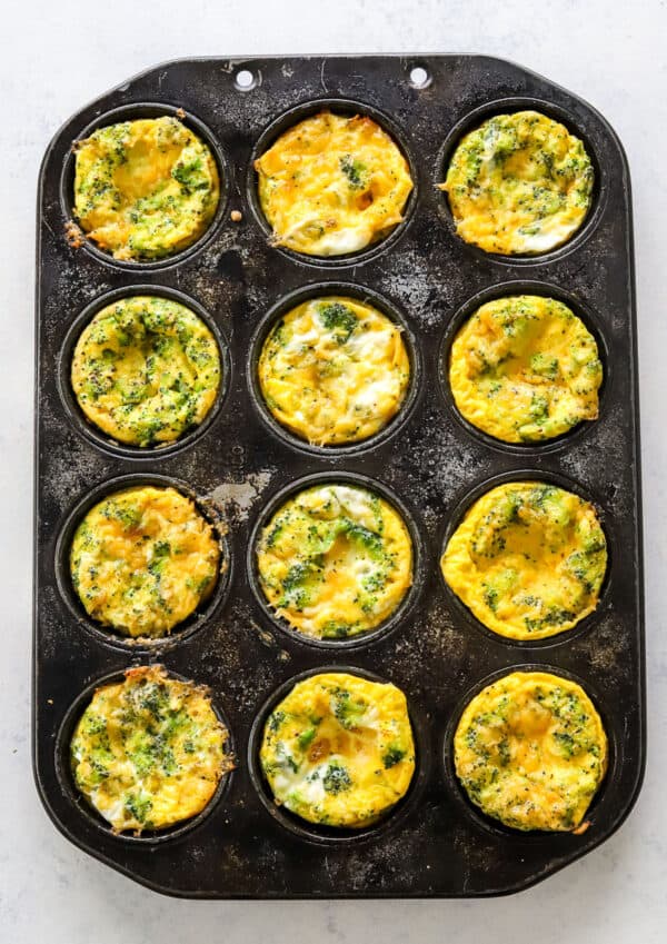Cooked broccoli and cheddar egg muffins in a dark muffin pan.