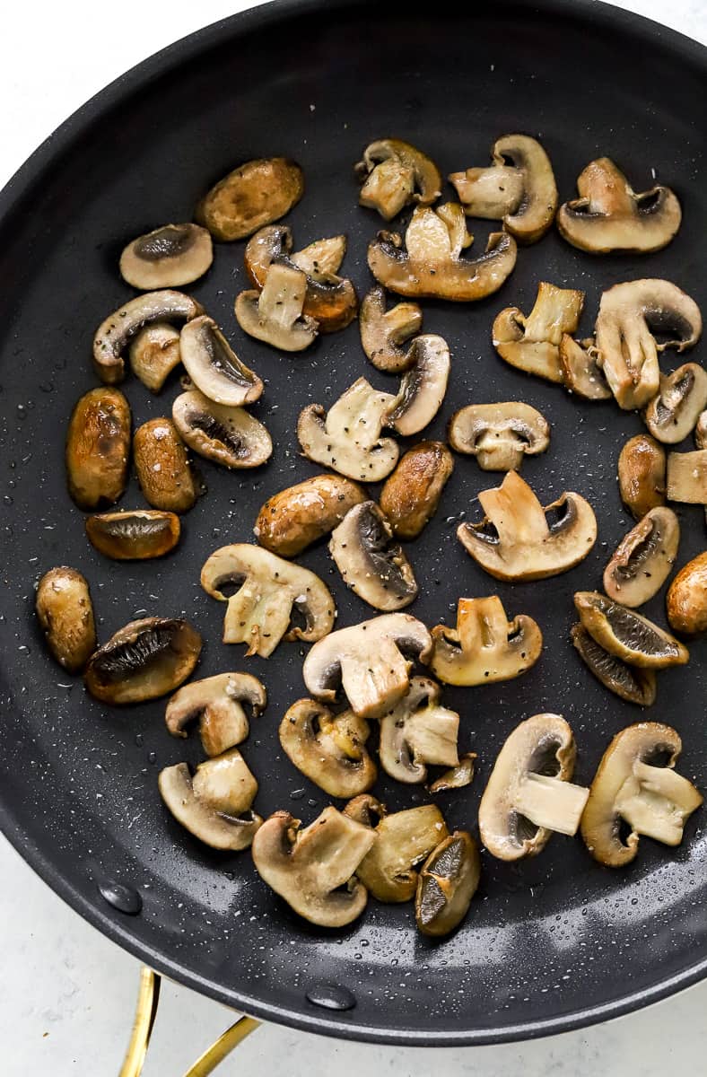 Sliced cooked mushrooms in a black sauté pan.