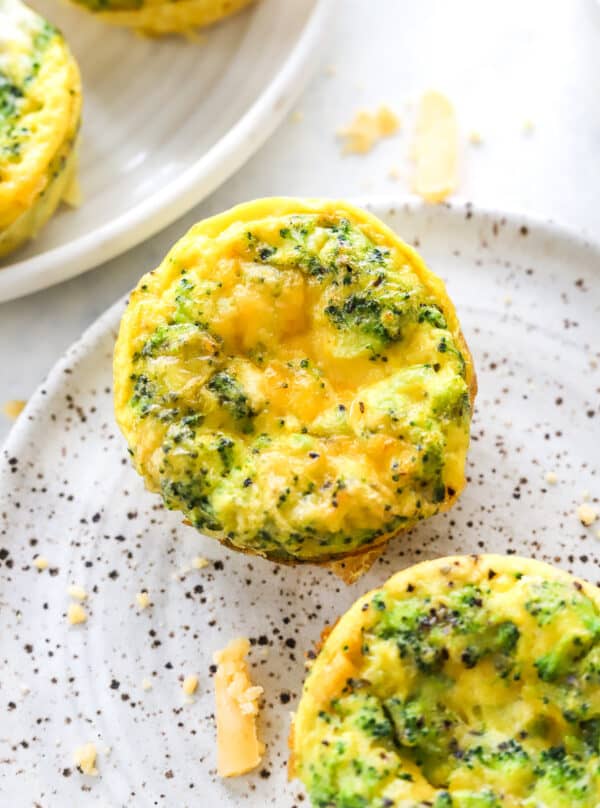Close up of a cheddar cheese and broccoli filled egg cup with another one in front of it and behind it.
