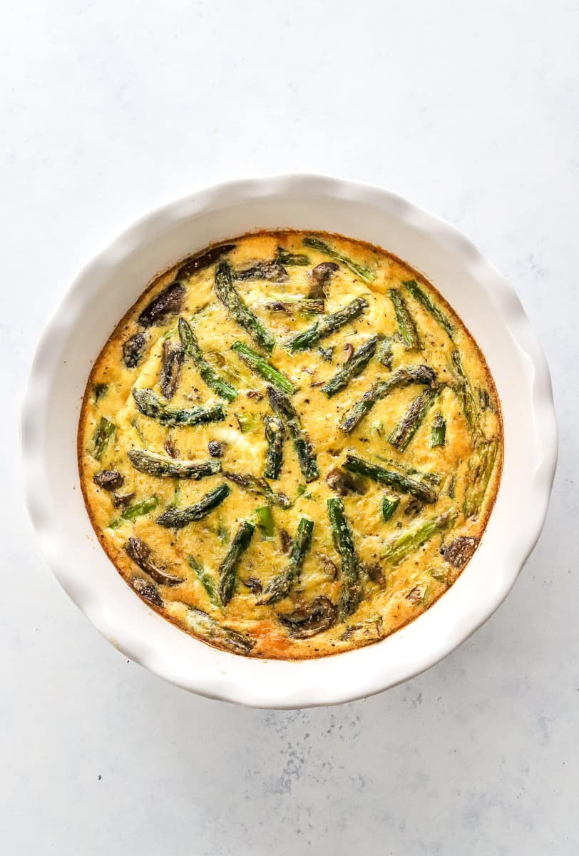 Baked quiche with asparagus and mushrooms in a white pie dish.