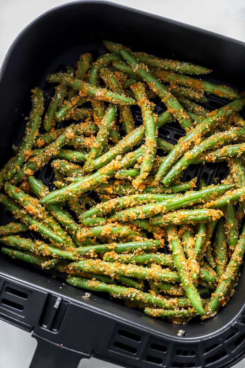 Coated raw green beans in a black air fryer basket.