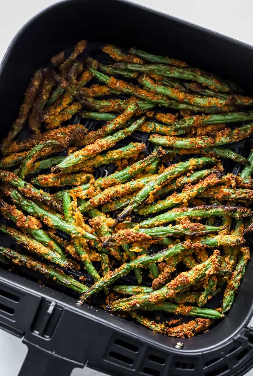 Crispy coated cooked green bean fries in an air fryer basket.
