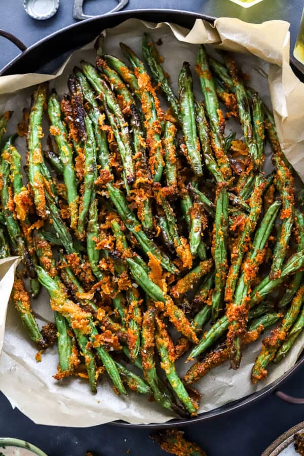 Round tin full of coated crispy green bean fries on top of parchment paper in the tin.