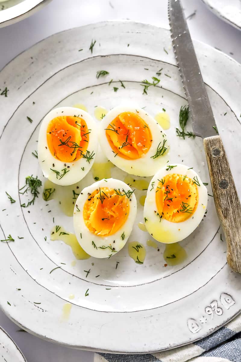 4 sliced air fryer hard boiled eggs on a plate topped with dill with a knife on the plate next to them. 