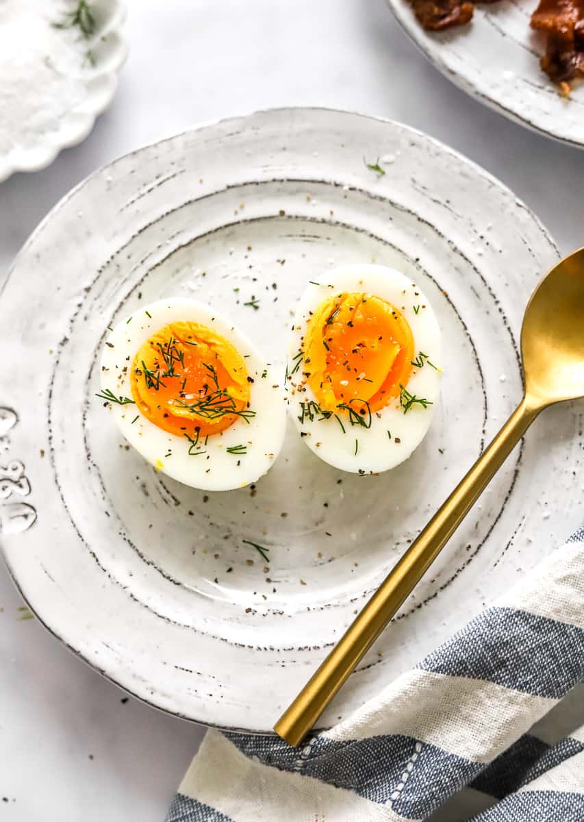 Slice air fryer hard boiled egg on a plate with herbs on it with a gold spoon in the plate. 