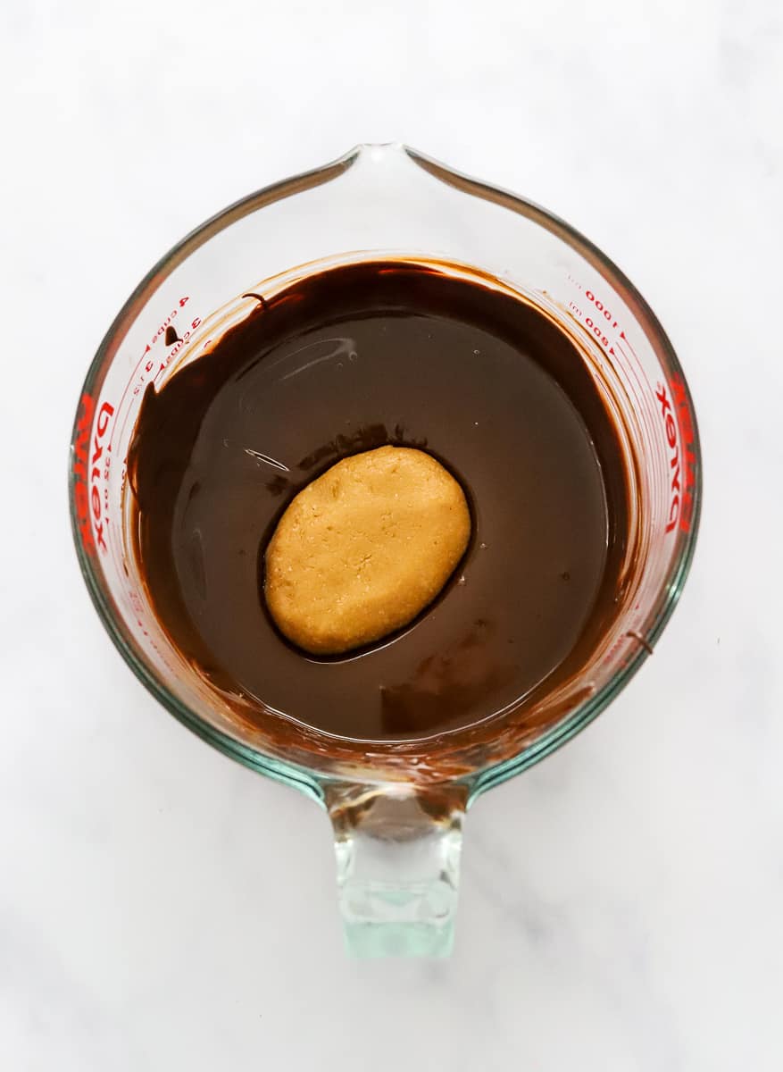 Melted chocolate in a glass pitcher with a formed peanut butter egg in the chocolate.
