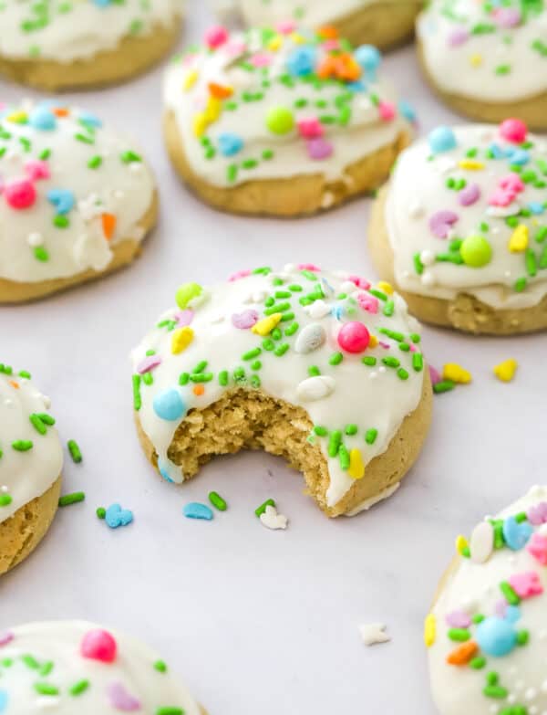 Close up of a thick easter cookie with white frosting and sprinkle on it with a bite taken out of it and more cookies around it.