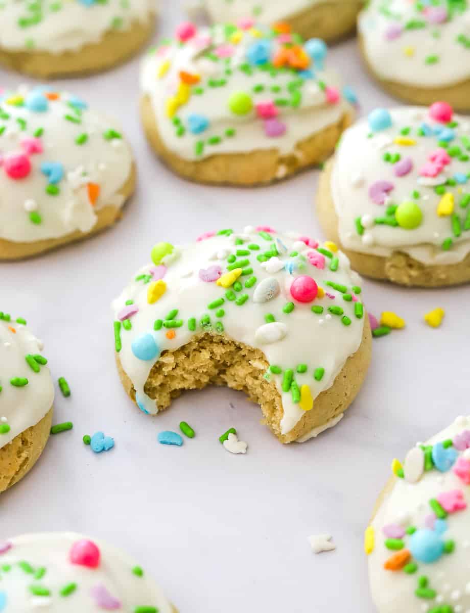 Close up of thick easter cookies with white frosting and sprinkle on it with a bite taken out of it and more cookies around it.