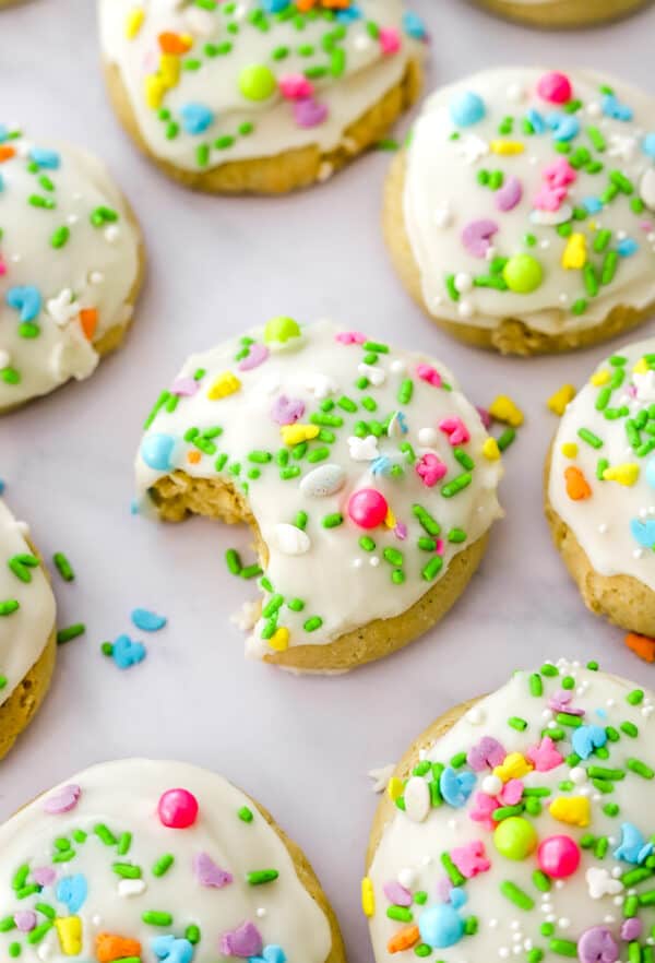 Round iced cookies with sprinkles on them with a bite taken out of the cookies in the middle.