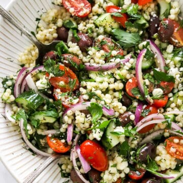 Large salad bowl filled with pearl couscous salat with tomatoes, herbs, onions and olive in it.