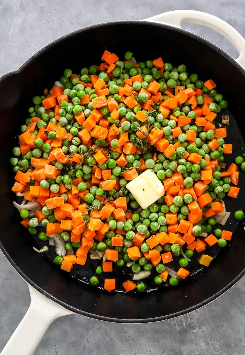 Frozen peas with diced carrots in a cast iron pan with a pat of butter on top of them.
