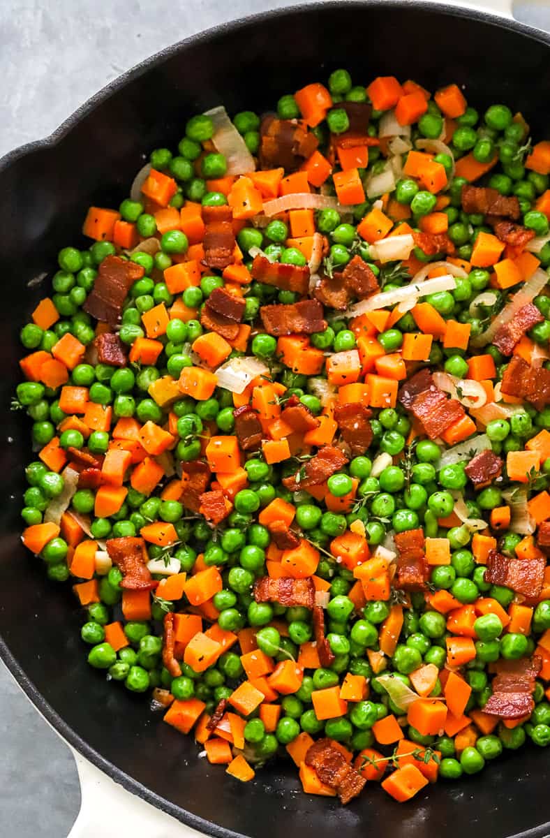 Peas and carrots with bacon, garlic and onion in a cast iron pan.