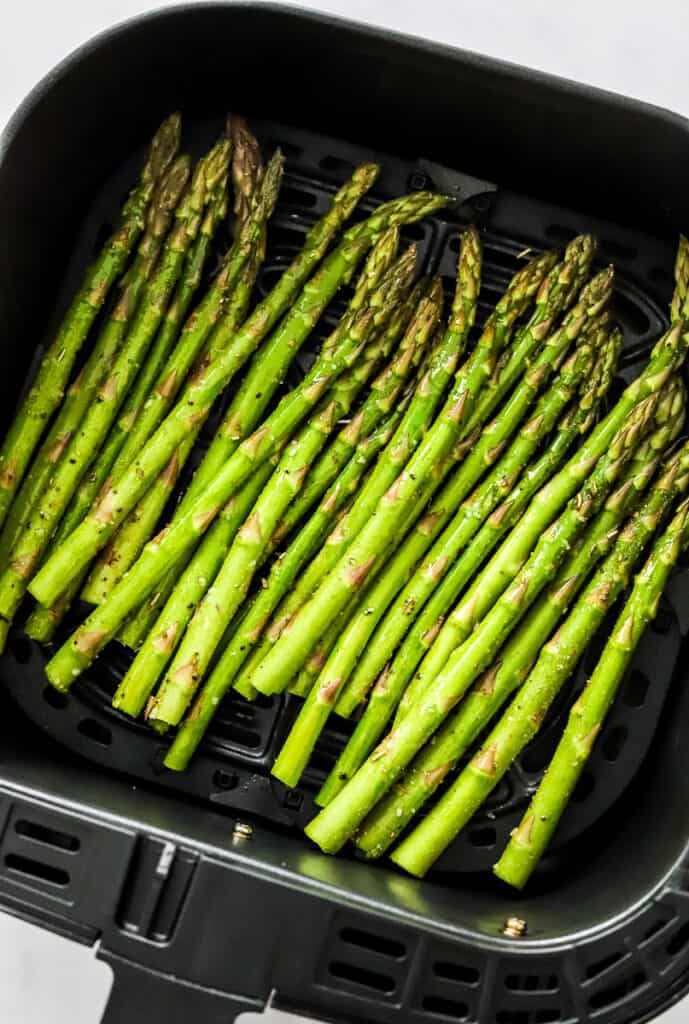 Raw, asparagus spears in a black air fryer basket. 