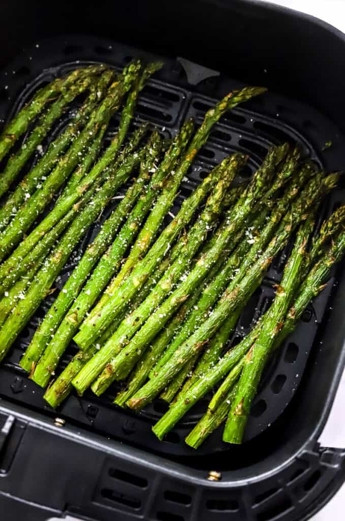Cooked, crispy asparagus in a black air fryer basket. 