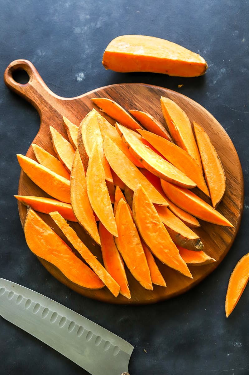 Sliced sweet potato wedges on a round wood cutting board with a knife next to them.
