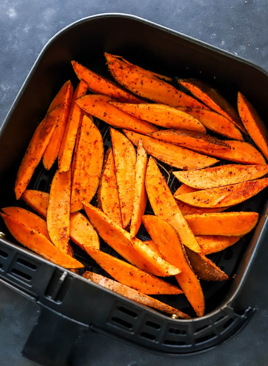 Seasoned, uncooked sweet potato wedges in a black air fryer basket.