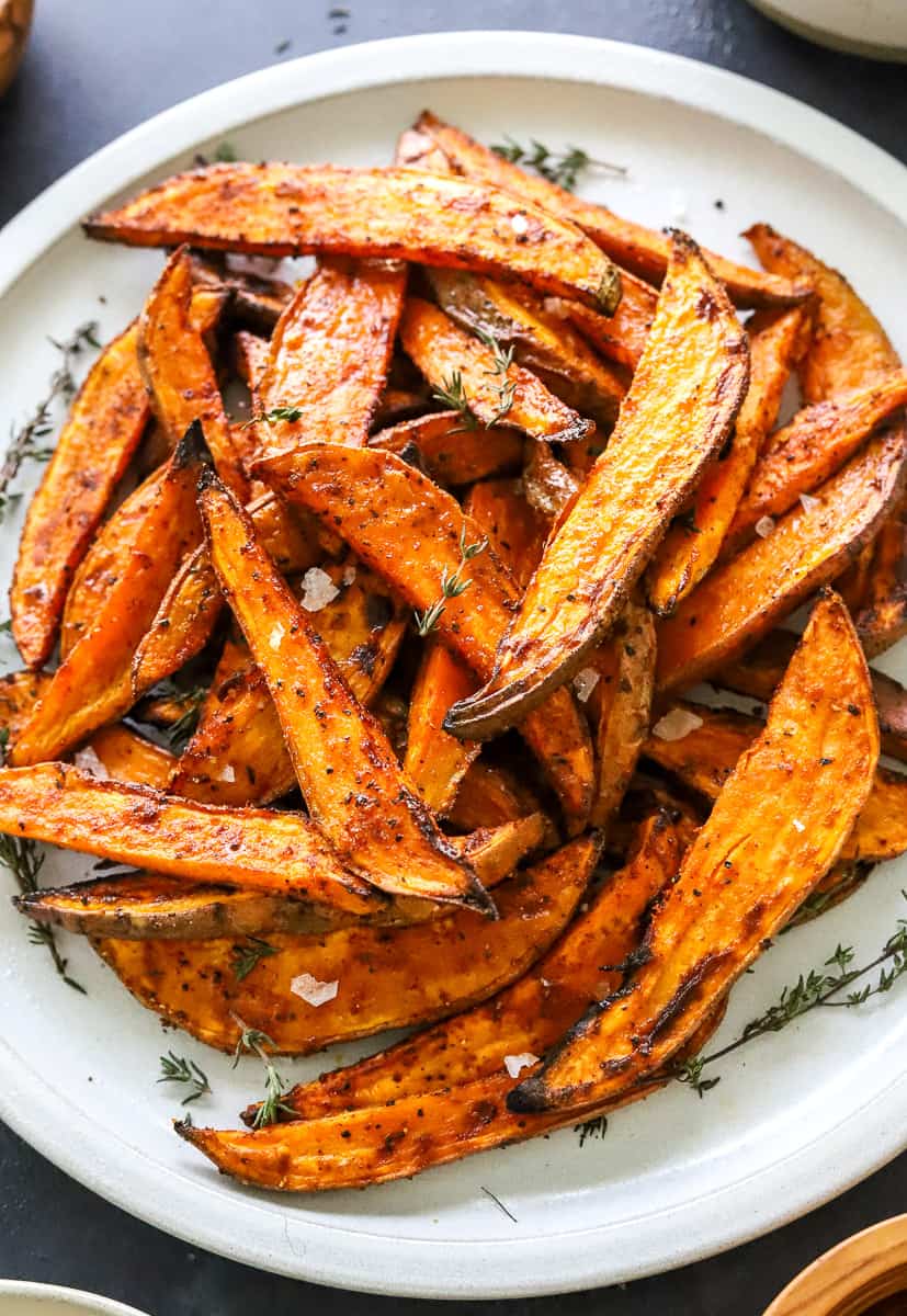 Sliced, cooked sweet potato fries on a plate with thyme and salt on them.