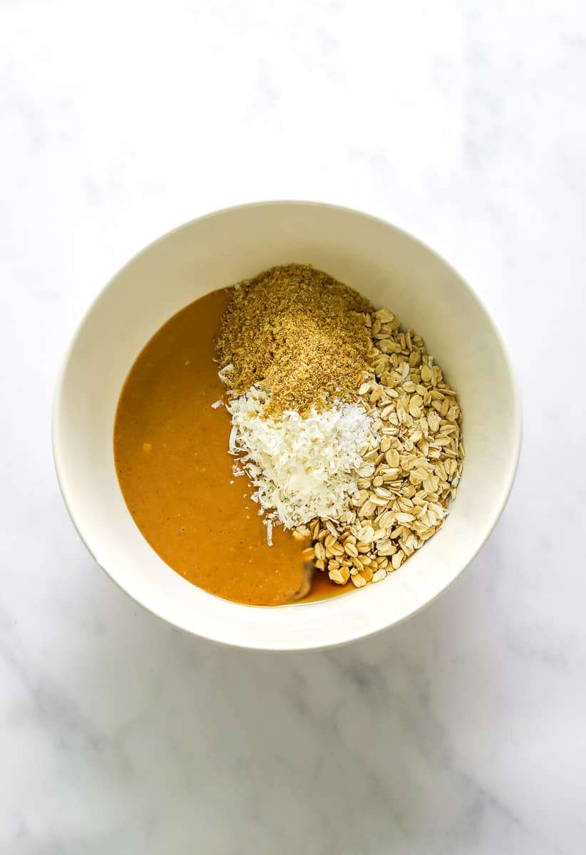 Creamy peanut butter, oats, ground flax seeds, shredded coconut in a white mixing bowl.