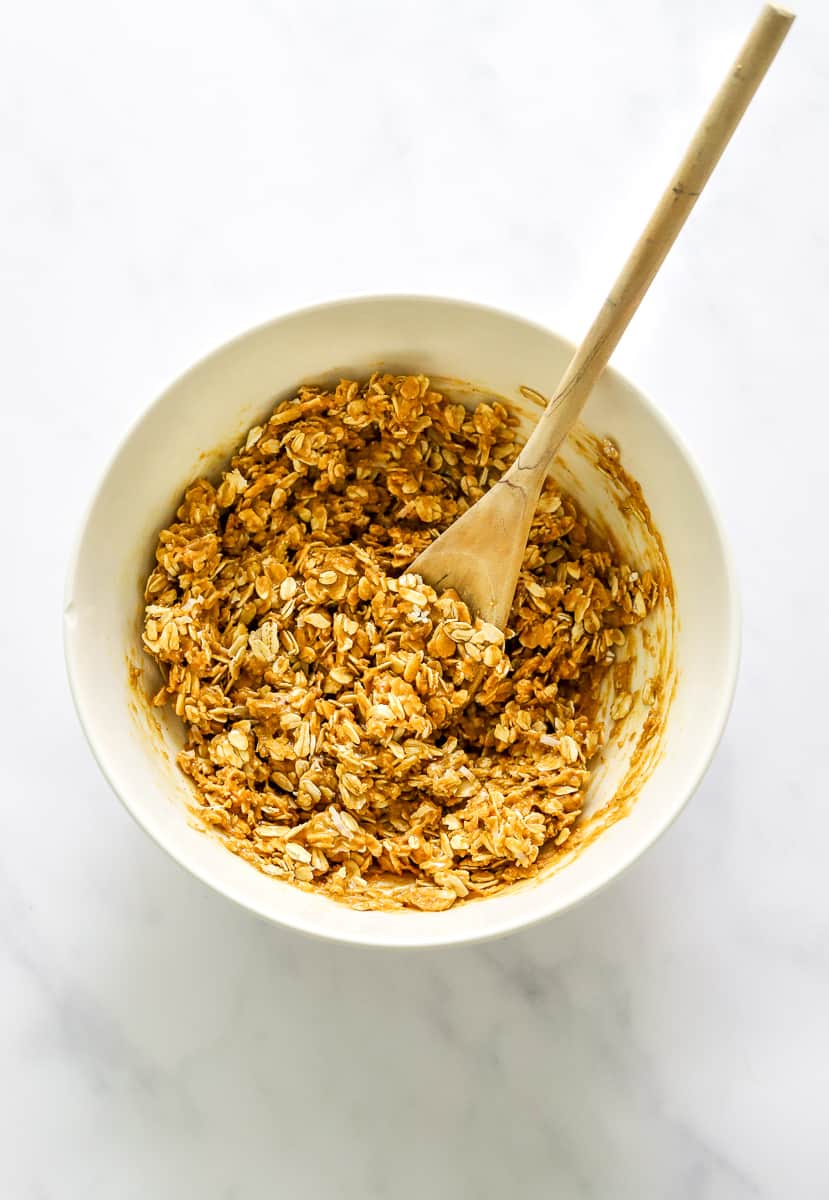 Mixed peanut butter oat mixture in a mixing bowl with a wooden spoon in the bowl.