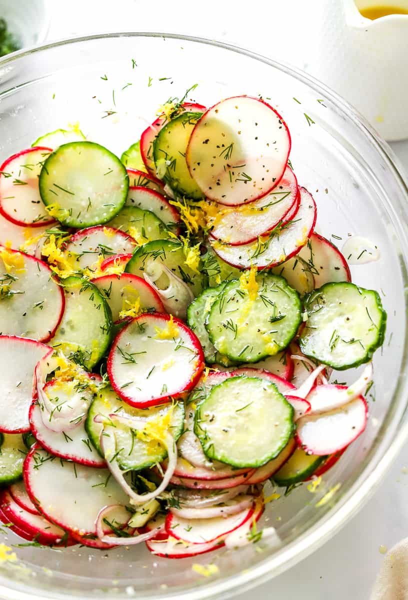 Cucumber radish salad with lemon and dill in an olive oil dressing tossed in a glass bowl. 