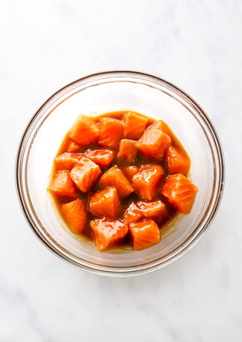 Raw cubed salmon tossed in teriyaki sauce in a round glass bowl.