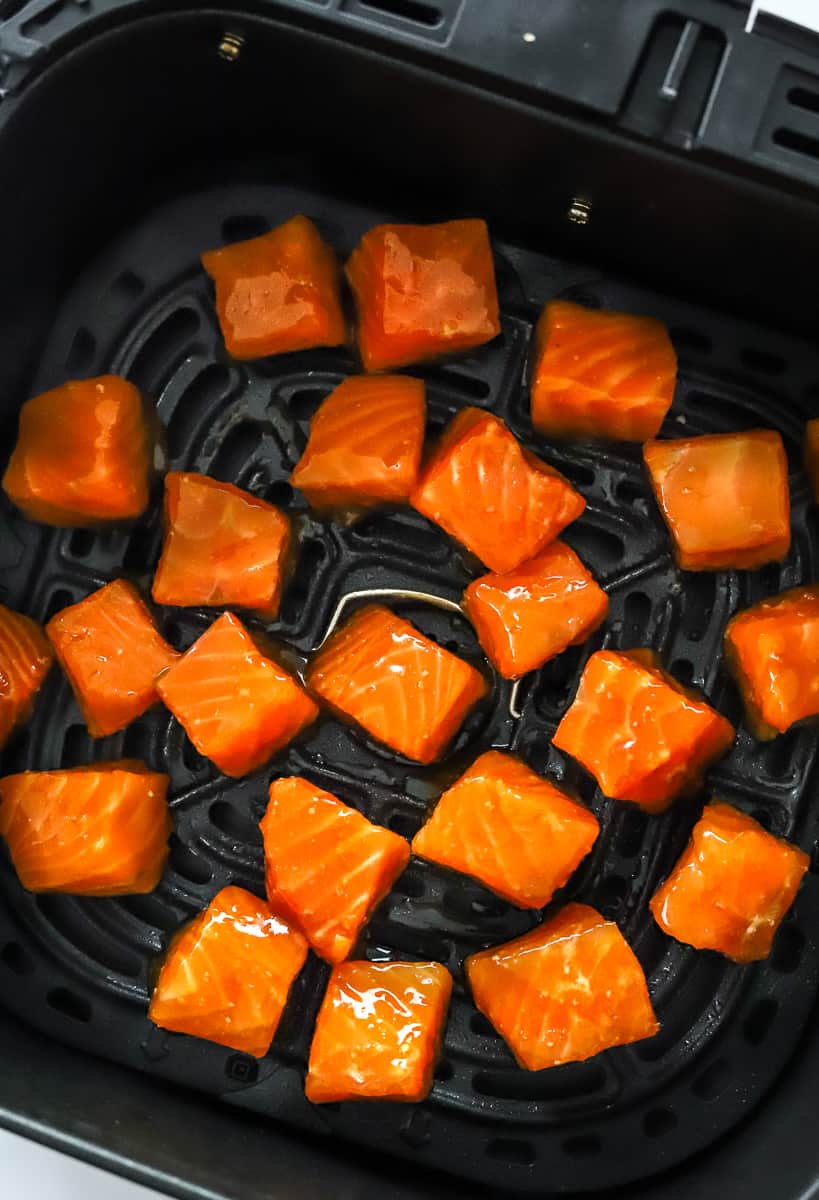 Marinated cubes of raw salmon in an air fryer basket.