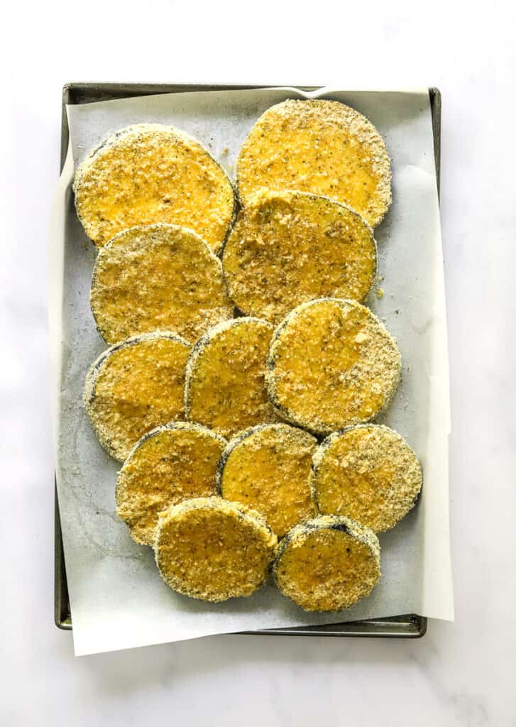Uncooked eggplant slices coated in breadcrumbs on a lined baking sheet 