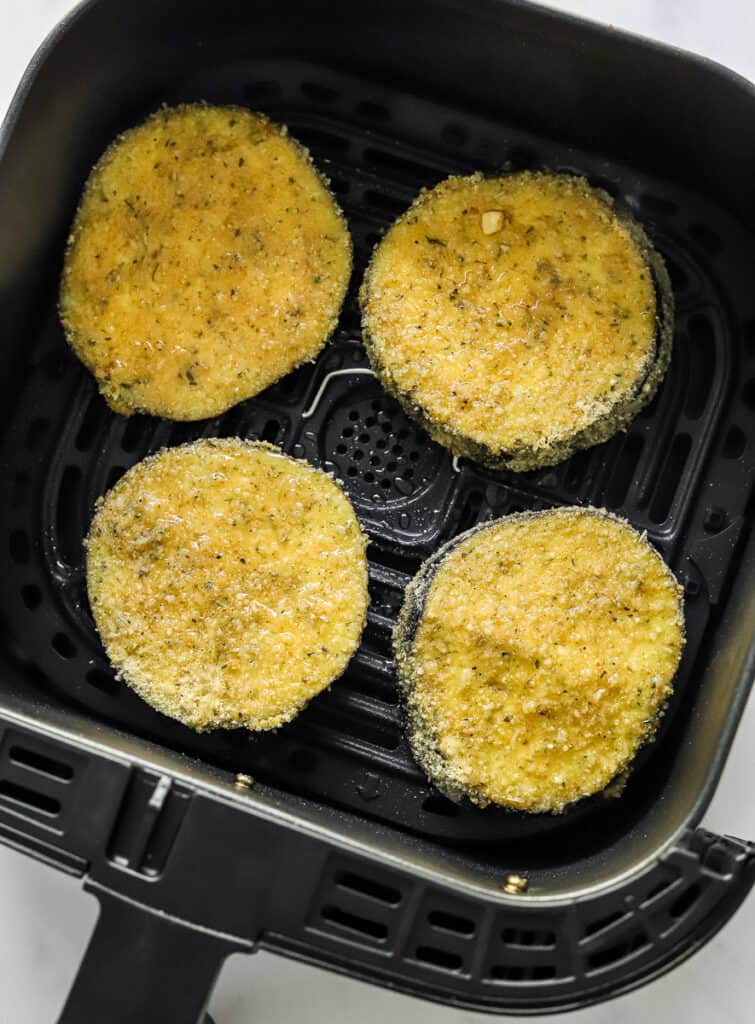 Uncooked coated eggplant slices in an air fryer basket. 