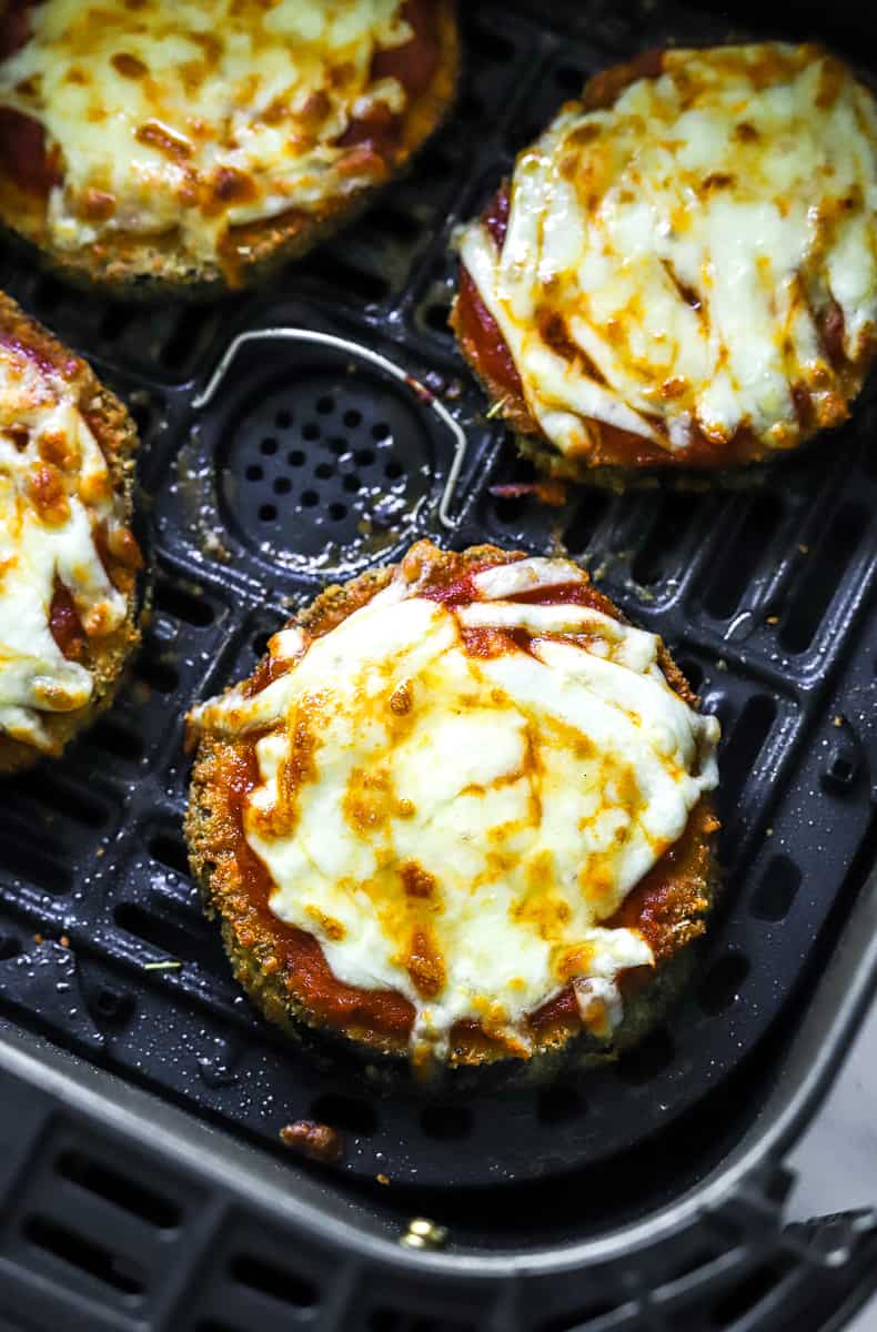 4 pieces of eggplant parmesan covered in sauce and melted cheese in an air fryer basket. 