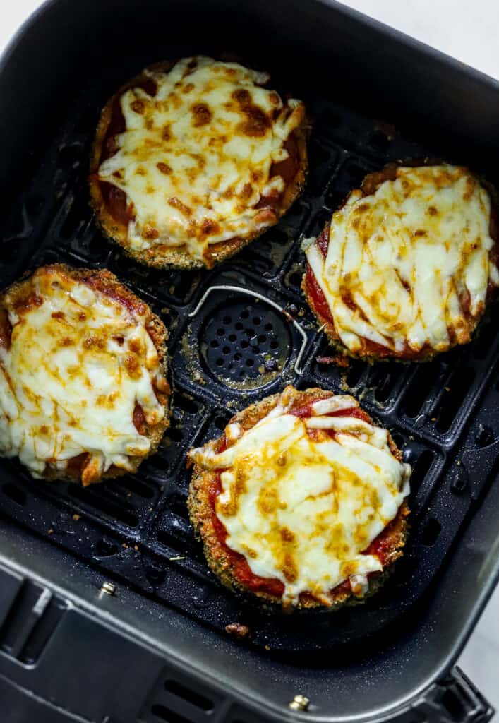 Cooked eggplant parmesan topped with melty cheese in an air fryer basket. 