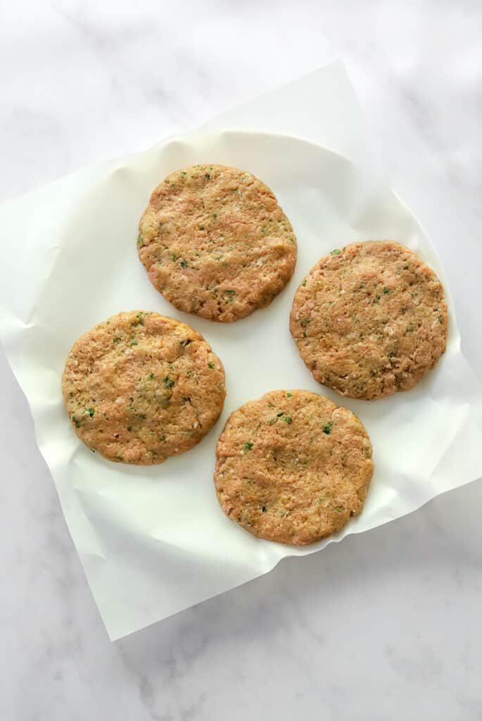 4 uncooked turkey burger patties on top of parchment paper on a plate. 