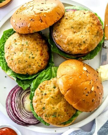 Plate of 3 air fryer turkey burgers on burger buns with let's and purple onion.