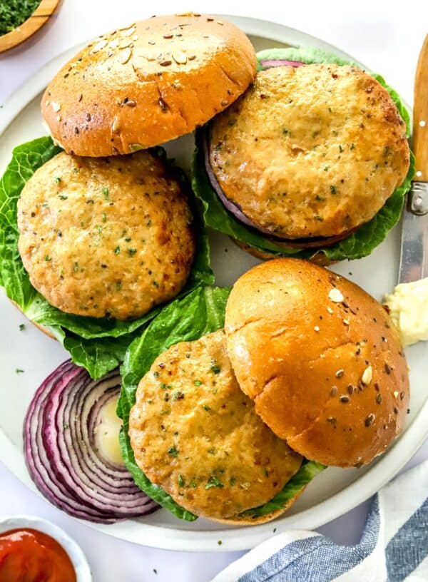 Plate of 3 air fryer turkey burgers on burger buns with let's and purple onion.