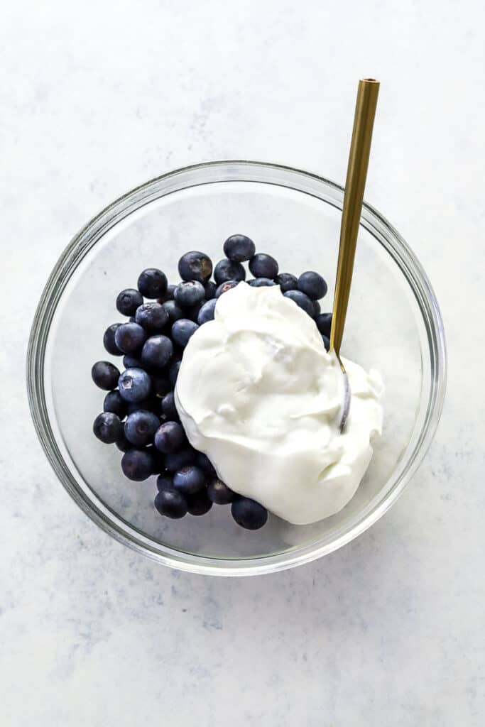 Bowl of blueberries with greek yogurt on top of it with a gold spoon in the bowl. 