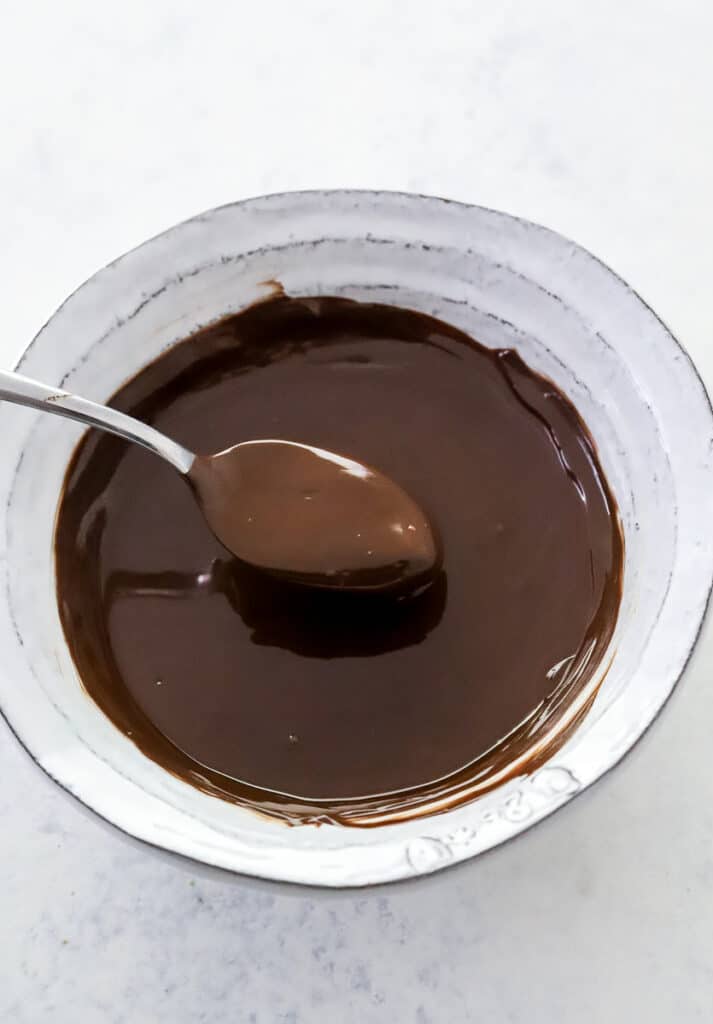 Bowl of melted dark chocolate with a spoon lifting out of the bowl. 