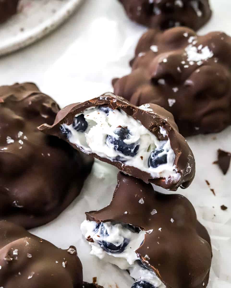 Blueberry yogurt clusters covered in chocolate with one cut open showing the inside and more behind it. 