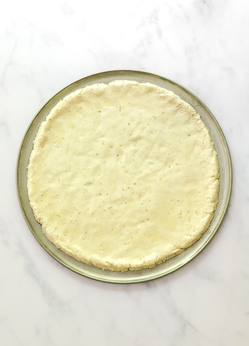Uncooked pizza dough spread out in a round pizza pan.