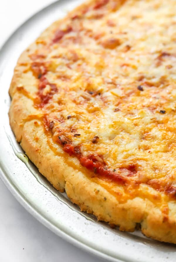 Close up of pizza topped with red sauce and cheese on a silver pizza pan.