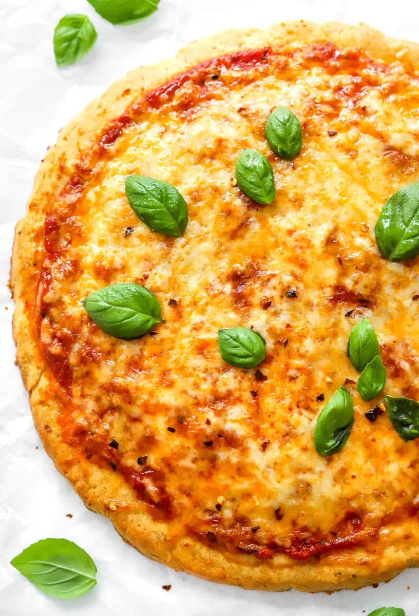 Golden cooked cheese pizza with basil on to of it with more basil leaves around it.