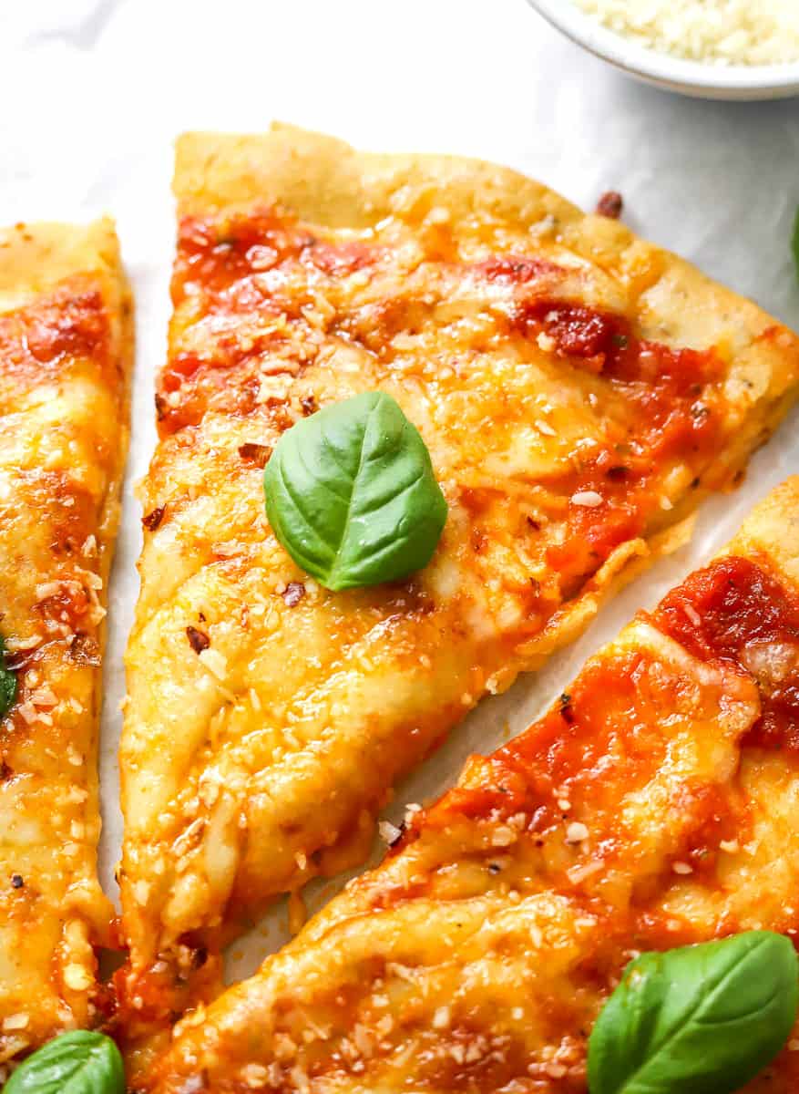 Slice of cheese protein pizza with a basil leave on it with more pizza on both sides of it.