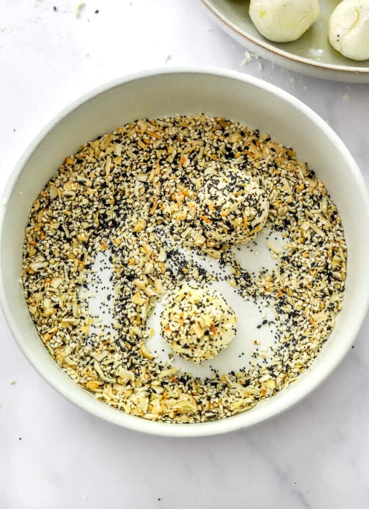 Bowl filled with everything bagel seasoning with two dough balls dipped in it with more dough balls behind it.