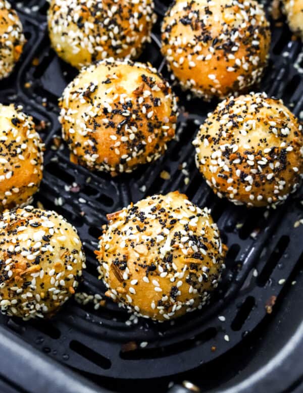 Close up of cooked mini bagel balls covered in everything seasoning in an air fryer basket.