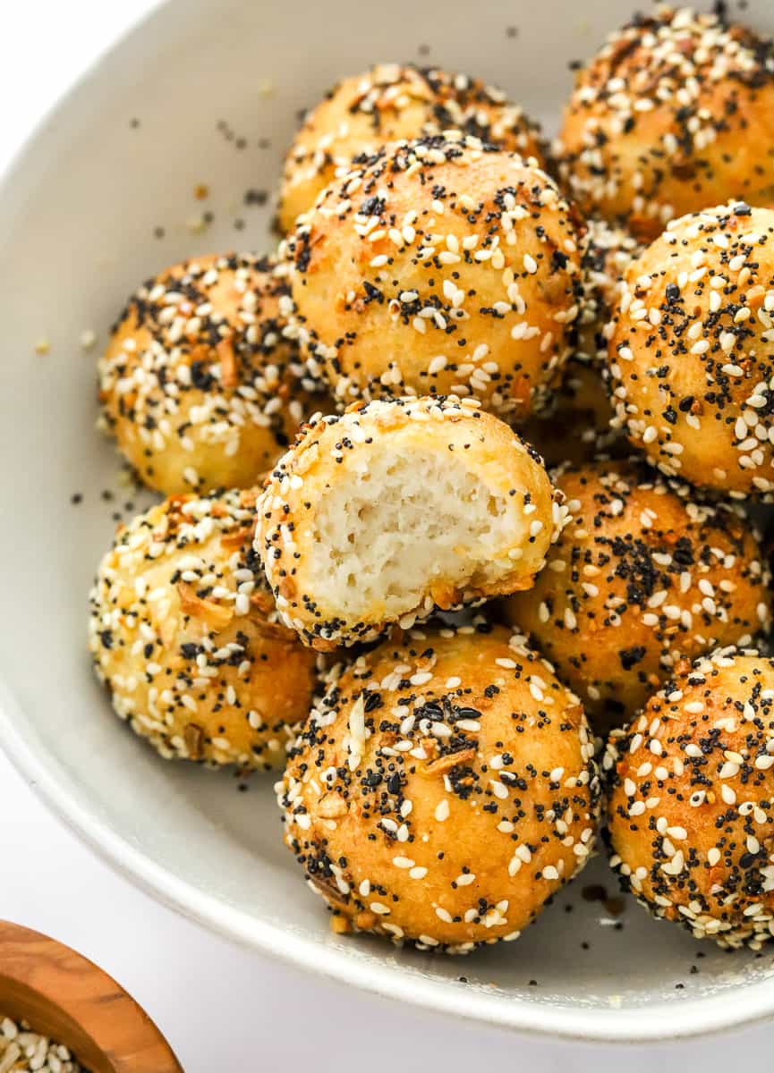 Bowl filled with bagel bites with seasoning on them with a bite taken out of one.