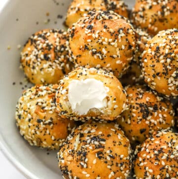 Everything bagel bites in a bowl with cream cheese spread on one of them.