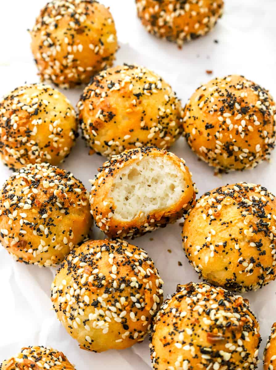 Cooked mini bagels with everything seasoning on them with a bite taken out of one of them on white parchment paper.