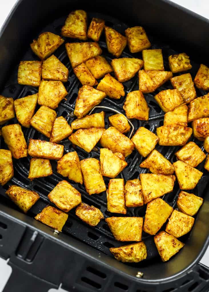 Chunks of golden glazed air-fried pineapple in a black air fryer basket.